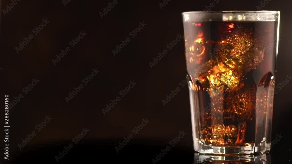 Coke with ice cubes closeup. Glass of fizzy cola rotated over brown background. Slow motion 4K UHD video footage. 3840X2160 Coke with ice cubes closeup. Glass of fizzy cola rotated over brown background. Slow motion 4K UHD video footage. 3840X2160