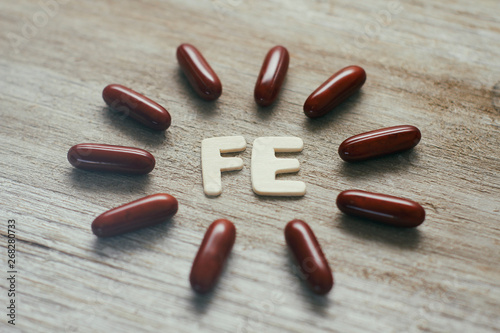 Dark red sleek capsules pills on wooden background. Iron concept. Ferrum inscription. Medical supplies.