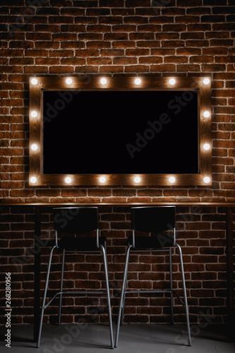 A makeup mirror with light bulbs  and wooden frame on a brown brick wall background with black space for text inside 