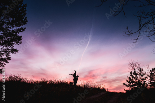 Silhouettes of a couple in love hug against a beautiful pink blue sunset in the forest