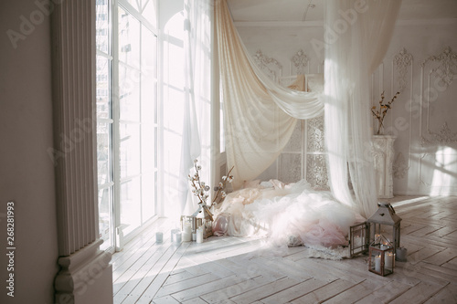 a large clean bright room with a window of white wooden floor, a mattress-bed, decorated with tulips curtains canopies, vases with cotton branches