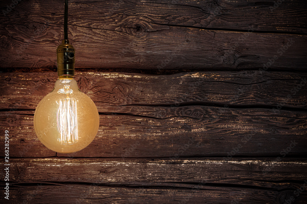 An old vintage electric light bulbs hanging in the air on the dark wooden background. Detail shot of a glass light bulb shining. Wall of wood and old light bulb.