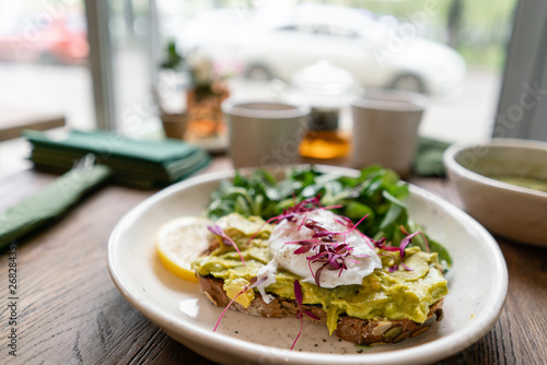 Morning in cafe, oak table. Healthy breakfast with wholemeal bread toast with avocado, poached egg with green salad. Green tea on the Background.