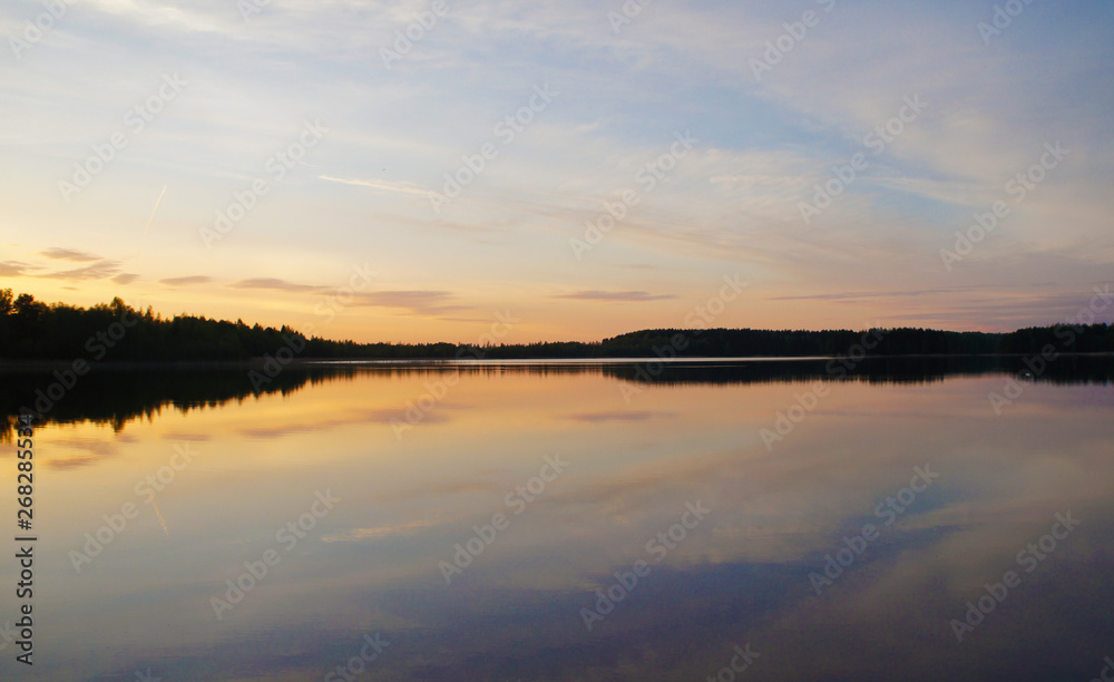 Beautiful sunset on the forest lake. The sun is reflected in the water. Bright contrasting sky.
