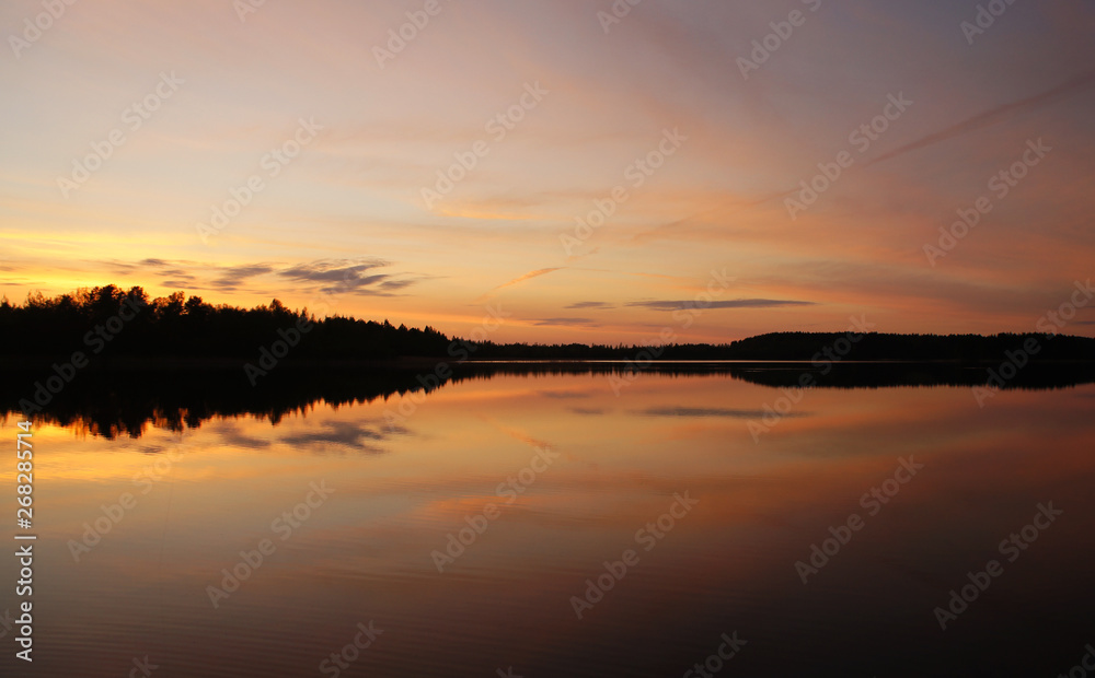 Beautiful sunset on the forest lake. The sun is reflected in the water. Bright contrasting sky.
