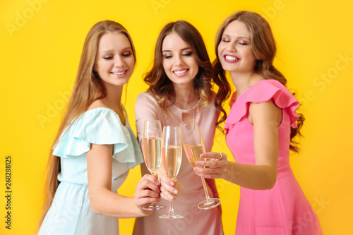 Beautiful young women drinking champagne on color background