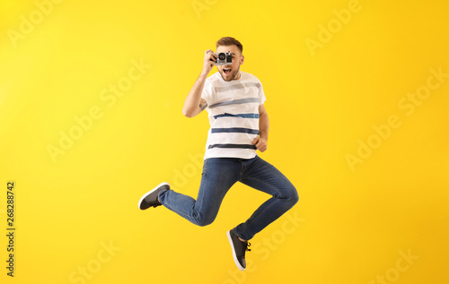 Fototapeta Naklejka Na Ścianę i Meble -  Jumping young man with photo camera on color background
