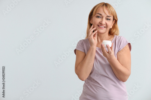 Mature woman with jar of cream on color background