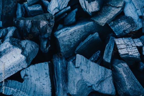 Black coals close up background. Burnt wood texture. Beams in grill, ashes in barbeque top view. Natural smouldering charcoal heap abstract backdrop. Grey firewood minimalistic composition