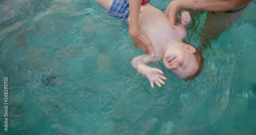 Young mother with 8 month old son in pool. Baby likes to swim. Woman bathes the baby holding him on his back on the surface of the water. in slow motion. Shot on Canon 1DX mark2 4K camera photo