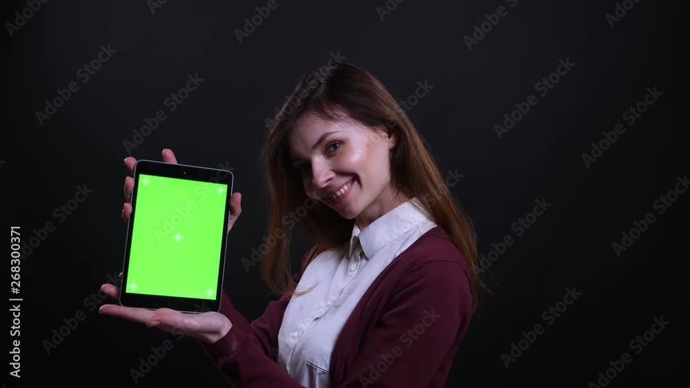 Portrait of young brunette businesswoman shows green chroma screen of tablet into camera on black background.