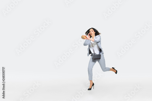 One moment. Young woman in gray suit comes late for work while talking with the boss on the run. Looking at watches while dropping coffee. Concept of office worker s troubles  business  stress out.