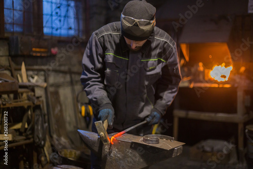 Professional blacksmith forging molten metal on anvil at smithy, workshop. Handmade, craftsmanship and blacksmithing concept