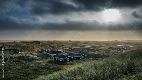 Abendstimmung über einer Ferienhaussiedlung in Dänemark, die Sonne scheint durch dunkle Wolken