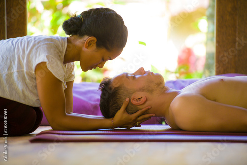 exotic Asian Balinese therapist woman giving traditional head and facial Thai massage to Caucasian man in harmony health care and wellness lifestyle at relaxing tropical spa photo