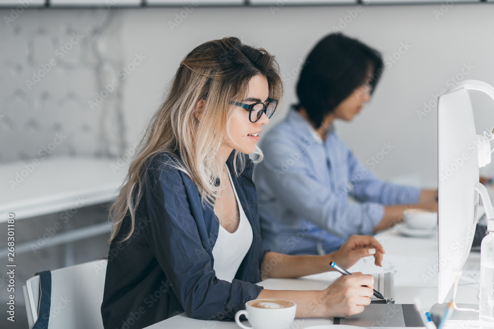 Busy female freelancer with long hair working with tablet and drinking coffee. Indoor portrait of concentrated japanese student using computer in classroom. Busy female freelancer with long hair working with tablet and drinking coffee. Indoor portrait of concentrated japanese student using computer in classroom.