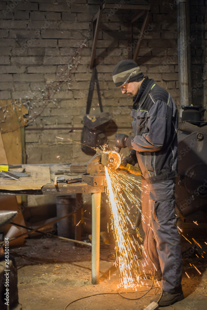 Professional blacksmith sawing metal with hand circular saw at forge, workshop. Handmade, craftsmanship and blacksmithing concept