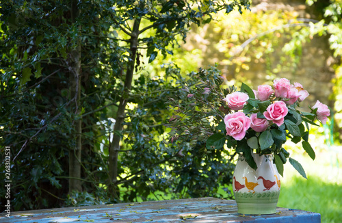 Fototapeta Naklejka Na Ścianę i Meble -  Vase of roses on blue wooden table in a garden