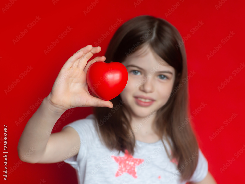 portrait of european smiling girl with heart in hand, concept of health, donations, childhood, valentine's day, isolated on red background portrait of european smiling girl with heart in hand, concept of health, donations, childhood, valentine's day, isolated on red background