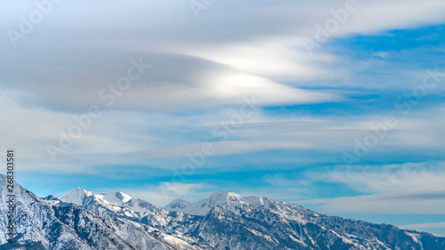 Panorama Striking mountain with rugged slopes under vast blue sky with clouds © Jason