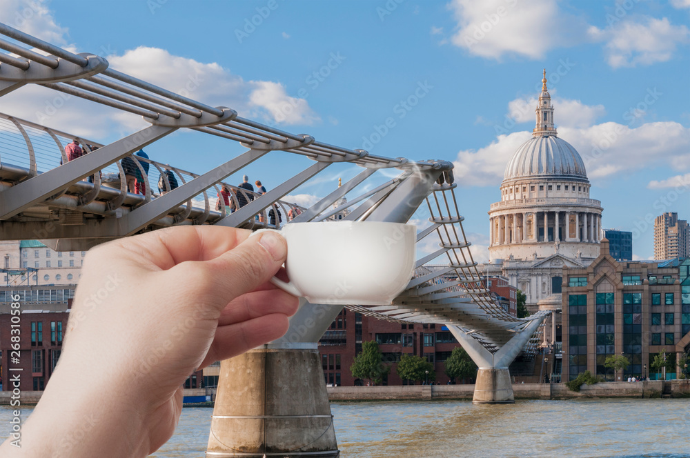 A man holding a cup of espresso coffee in front of the millennium bridge and the St. Paul chatedral in London