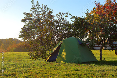 Green camping tent on the grass at sunset
