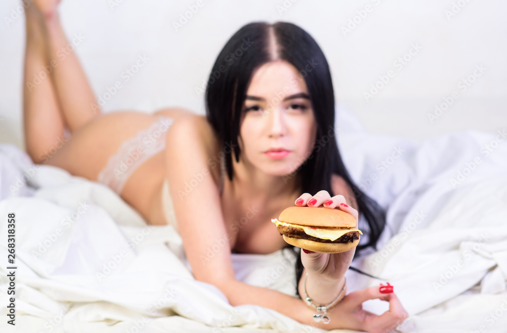 Girl in sexy lingerie eat burger. Sexual appetite. Food delivery service.  Seductive sexy woman relax on