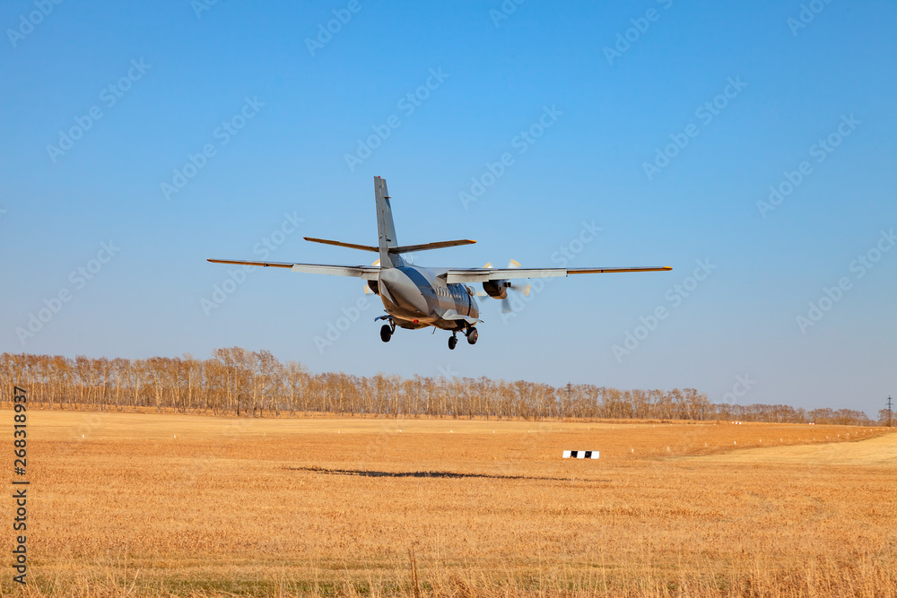 A small aircraft for the transport of passengers and paratroopers lands in a field on a landing strip with grass under a blue sky above the trees on a clear cloudless day. Air patrol. A small aircraft for the transport of passengers and paratroopers lands in a field on a landing strip with grass under a blue sky above the trees on a clear cloudless day. Air patrol.