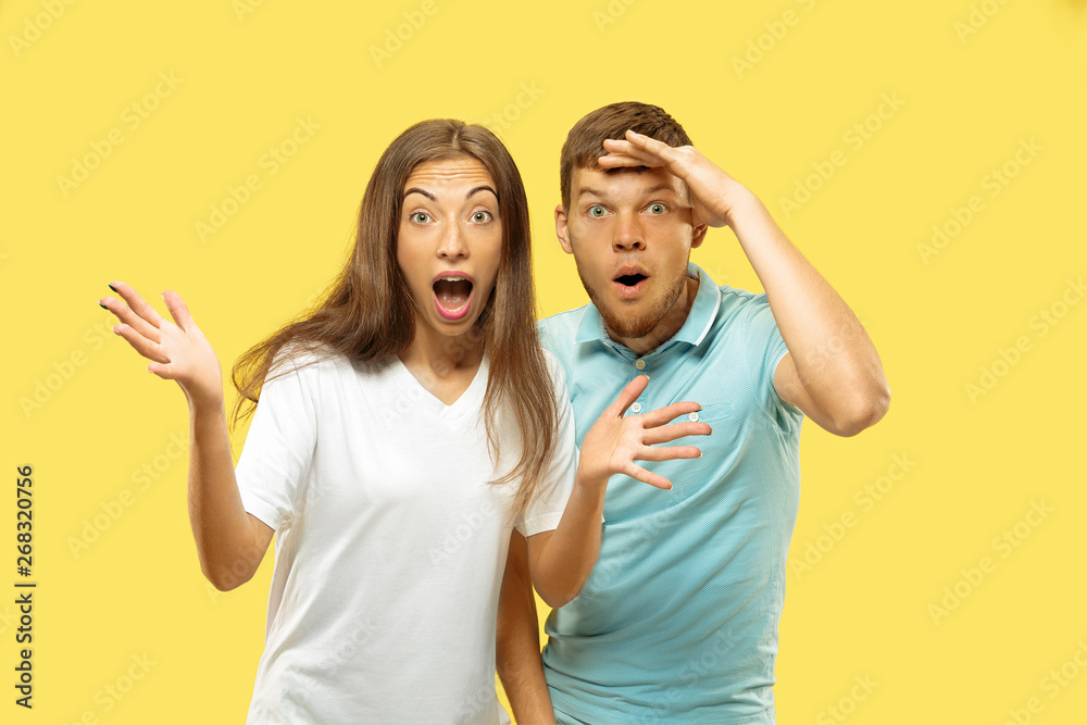Fototapeta premium Beautiful young couple's half-length portrait on yellow studio background. Woman and man in shirts looking for something and wondering. Facial expression, human emotions concept. Trendy colors.