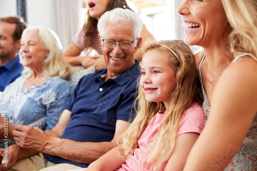 Multi-Generation Family Sitting On Sofa At Home Watching Movie Together