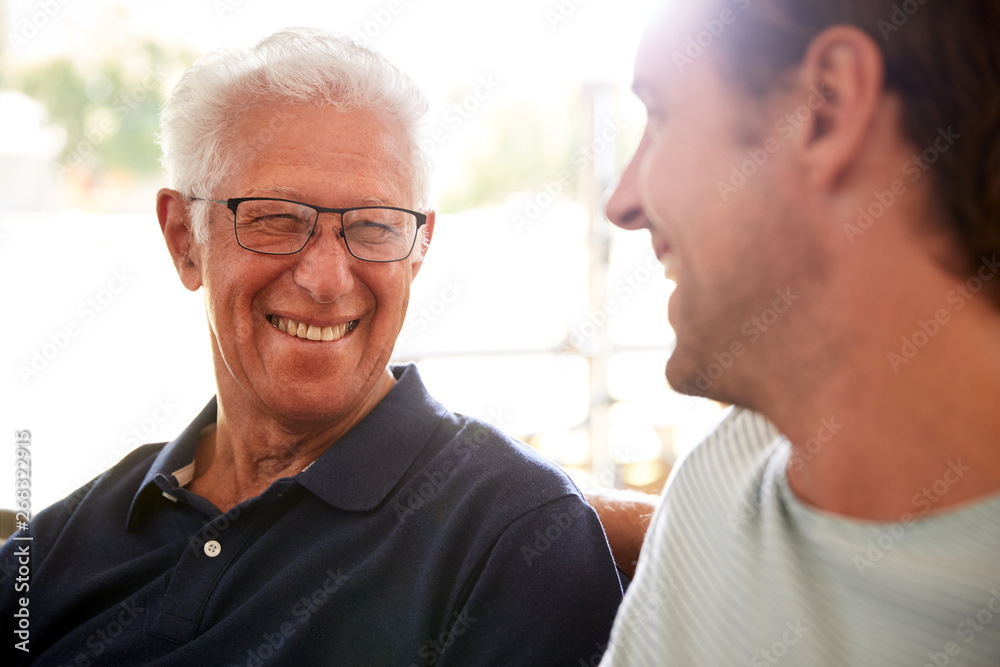 Smiling Father With Adult Son Relaxing On Sofa At Home Smiling Father With Adult Son Relaxing On Sofa At Home