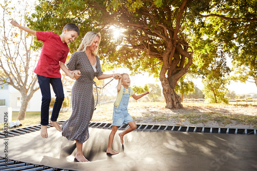 Mother Playing With Children On Outdoor Trampoline In Garden photo