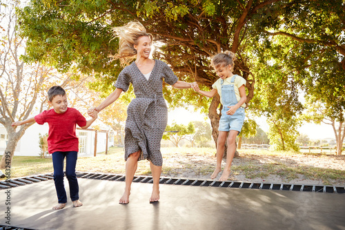 Photography Mother Playing With Children On Outdoor Trampoline In Garden