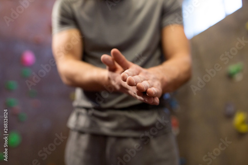 fitness, extreme sport, bouldering, people and healthy lifestyle concept - close up of male climber drying hands by talc at indoor climbing gym