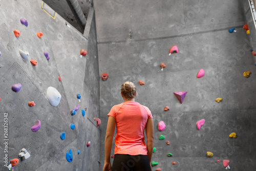 fitness, extreme sport, bouldering, people and healthy lifestyle concept - young woman at indoor climbing wall in gym from back