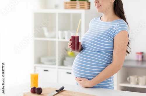 healthy eating, pregnancy and people concept - pregnant woman drinking fruit smoothie at home kitchen