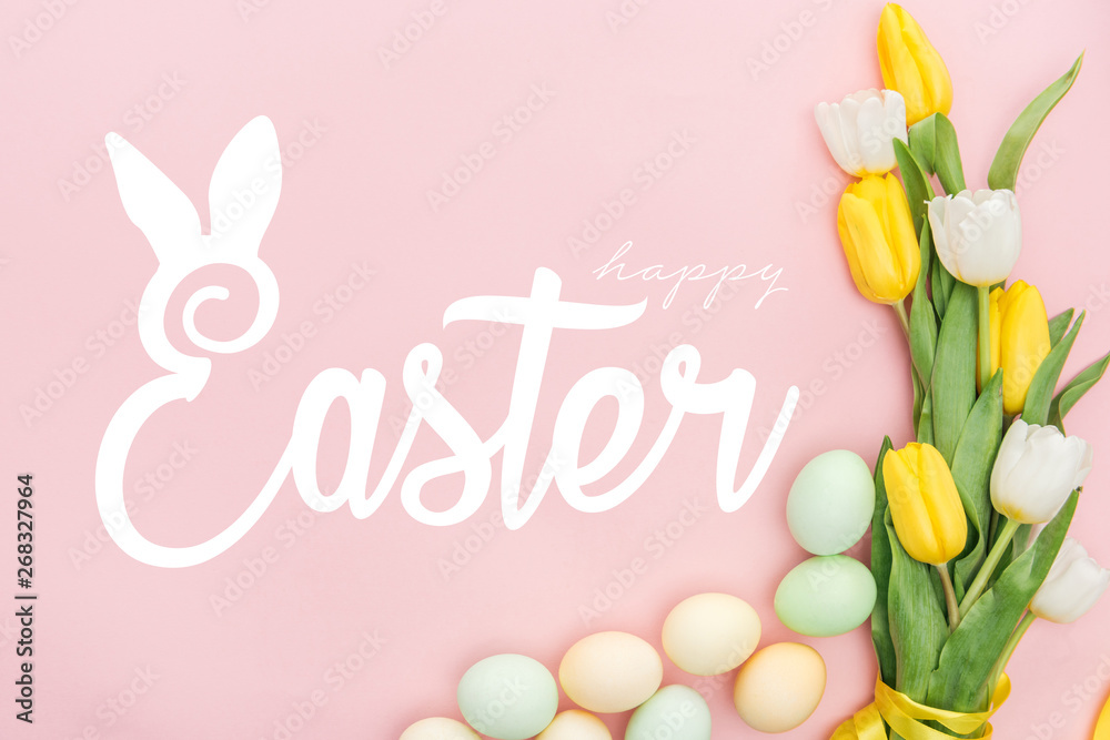 top view of painted chicken eggs and bright tulips on pink background with happy Easter lettering