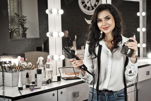 The girl in the beauty salon. Brunette hairdresser on background of mirror with backlight. Master with tools and cosmetics.