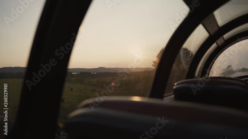 Farms, fields, landscapes and a small city seen from a sightseeing train (the seats of the train are also shown) - panoramic view during sunrise - slow motion.