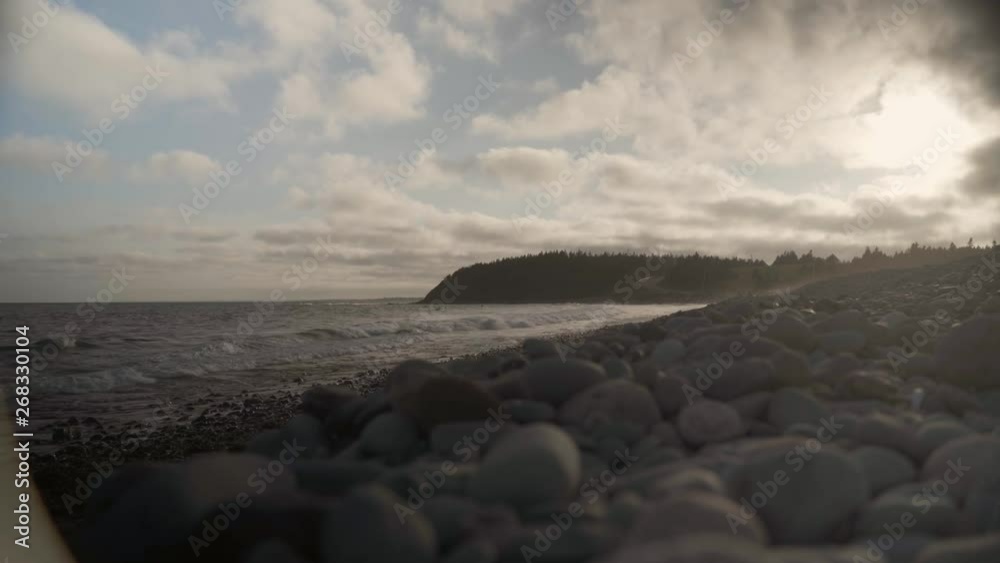 Ground shot of some waves hitting beach with some stones on the ground, trees and a road on the background near sunset in Halifax, Nova Scotia, Canada. Ground shot of some waves hitting beach with some stones on the ground, trees and a road on the background near sunset in Halifax, Nova Scotia, Canada.