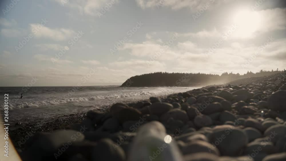 Ground shot of some waves hitting beach with some stones on the ground, trees and a road on the background near sunset in Halifax, Nova Scotia, Canada. Ground shot of some waves hitting beach with some stones on the ground, trees and a road on the background near sunset in Halifax, Nova Scotia, Canada.