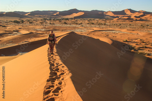 The highest sand dunes in the world at sunset in Namib Desert  in the Namib-Nacluft National Park in Namibia. Sossusvlei. Young woman tourist with backpack stands on top
