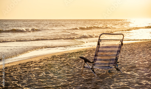 Aluminum striped deckchair at ocean sandy beach with sunset light
