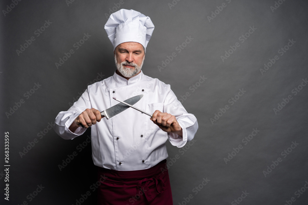 Portrait of a mature chef cook holding knifes isolated on a black background. Portrait of a mature chef cook holding knifes isolated on a black background.