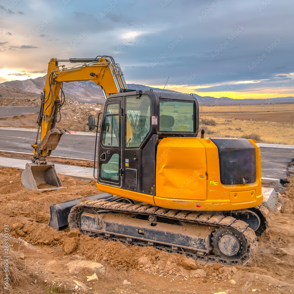 Excavator on the side of the road against a rugged mountain and dramatic sky Excavator on the side of the road against a rugged mountain and dramatic sky