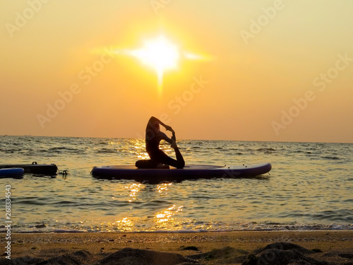 young happy girl woman doing yoga at sea on a SUP water board. Meditation. Beautiful dawn. Sport health holidays