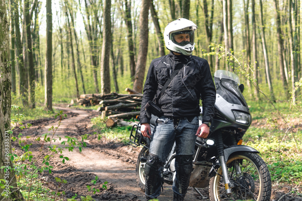 Motorcyclist man stands with his Adventure Motorbike. Off road. Motorcycle trip. enduro Traveling, Lifestyle Travel dual sport outdoor concept. clothing with protection, forest background