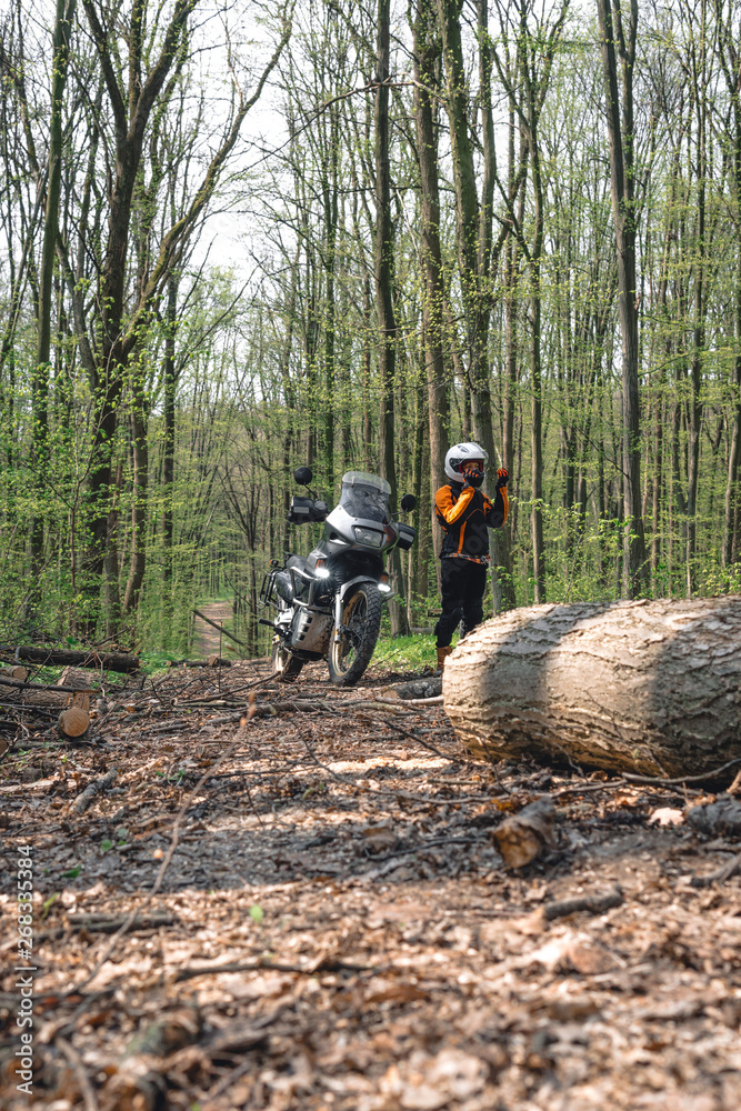 Biker girl wearing a motorcycle outfit, protective clothing, equipment, adventure touristic motorbike. outdoor travel, Forest path with fallen trees, logs, after a strong wind the road is blocked