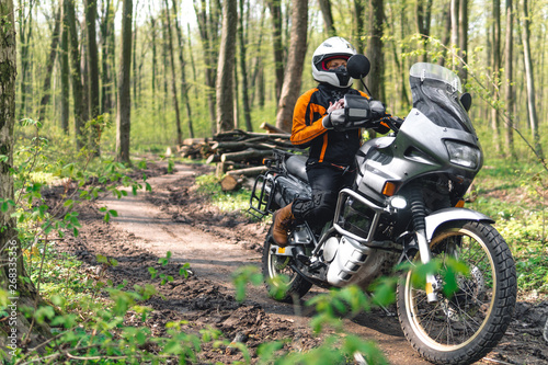 Biker girl wearing a motorcycle outfit, protective clothing, equipment, adventure touristic motorbike with side bags. outdoor travel, off road enduro active traveler, sunny forest