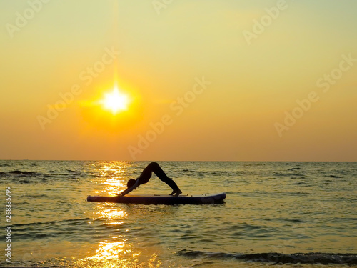 young happy girl woman doing yoga at sea on a SUP water board. Meditation. Beautiful dawn. Sport health holidays